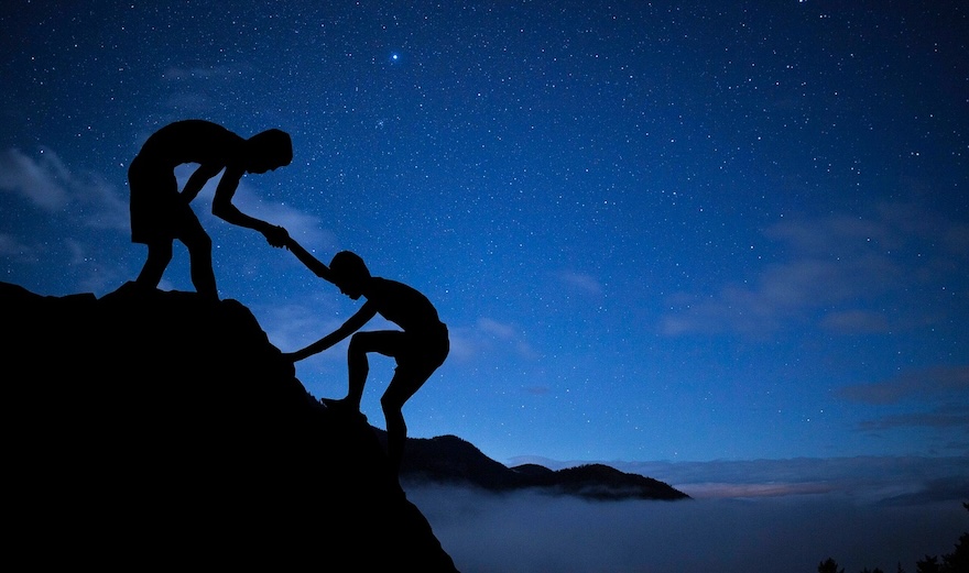 man helping another man climb up mountain